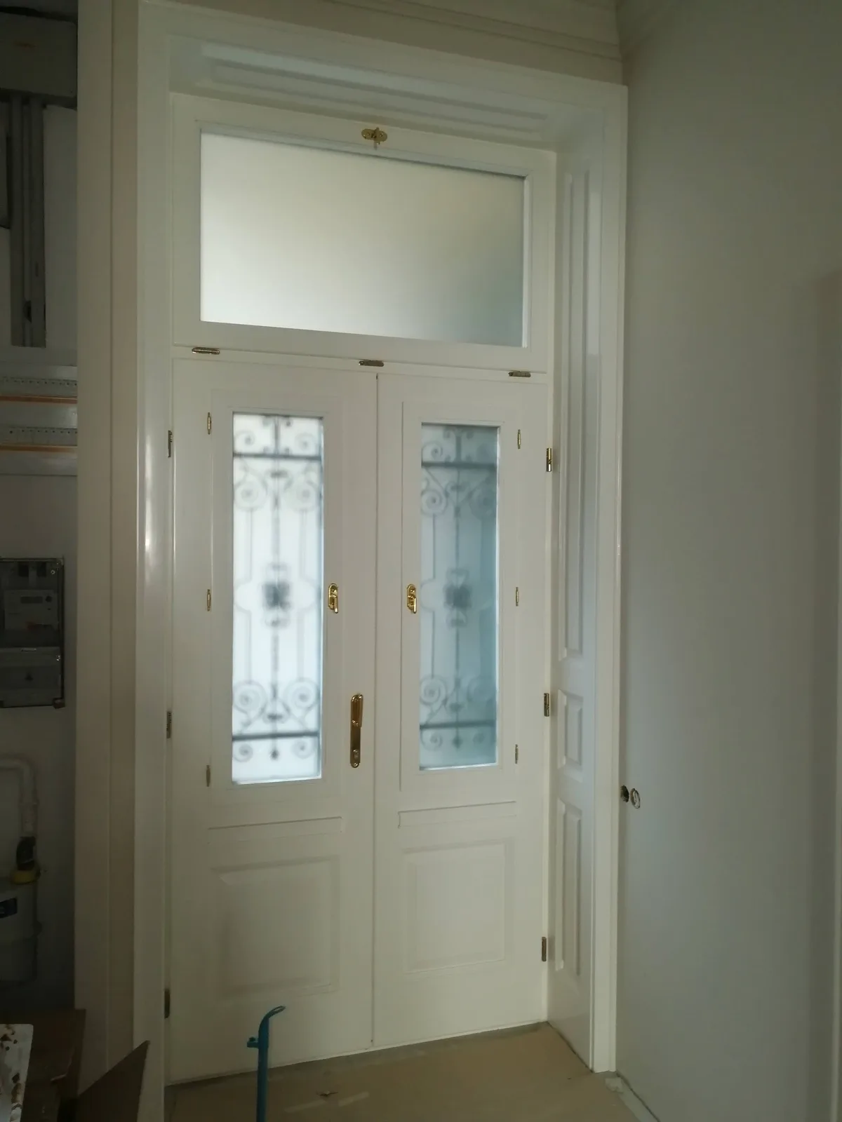 Körfolyosós társasházi bejárati ajtó igazi kovácsoltvas ráccsal, az ajtóban nyitható ablakokkal. Felül bukó kivitelű, kitámasztóval, hőszigetelt üveggel, dupla gumiszigeteléssel, réz kilincsekkel, belül fehérre fényezve, kompletten, beépítéssel együtt. Kazettás beltéri ajtó monarchia rézkilincsekkel, fehérre fényezve.
